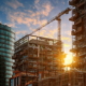 Construction site with tower crane and scaffolding at sunset, builders specifying building materials